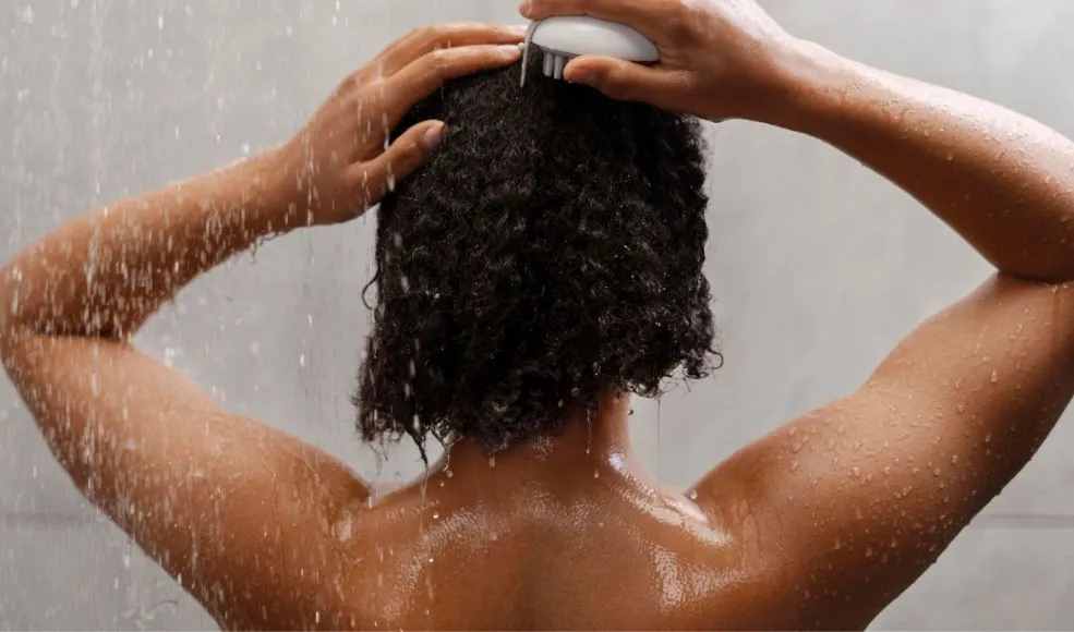 Black woman rinsing her hair in the shower with water running down her hair and back