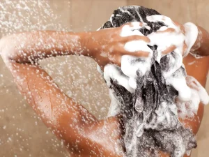 A black woman washing her hair with lathered up shampoo in the shower