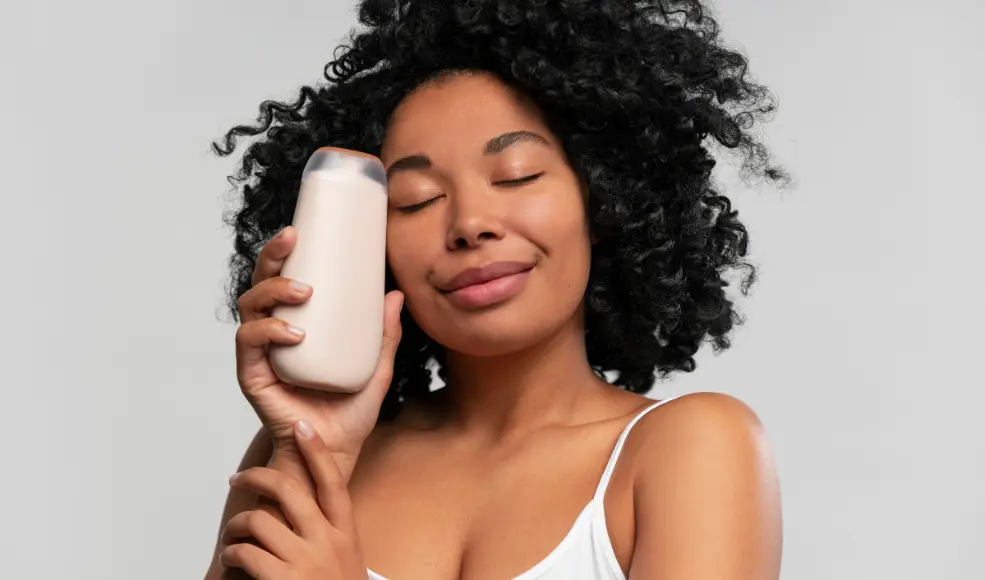 A woman holding a plain bottle of shampoo to her face and smiling with her eyes closed